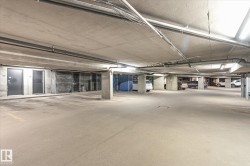 Underground concrete parking garage featuring ample parking spaces, exposed utility conduits, and integrated ceiling lighting - 
