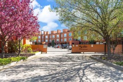 Gated community entrance with mature landscaping, featuring a vibrant pink flowering tree and green foliage - 