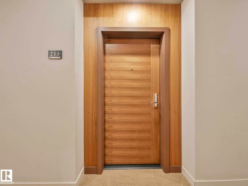 Wood-finish entry door with brushed chrome hardware, framed by wood-paneled walls and neutral painted surfaces - 213 625 Leger Way, Edmonton, AB - Indoor Photo Showing Other Room