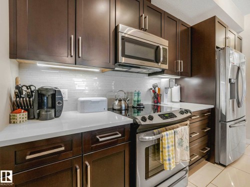Modern kitchen featuring dark wood-finish cabinetry with brushed nickel hardware, white countertops, and a white subway tile backsplash - 213 625 Leger Way, Edmonton, AB - Indoor Photo Showing Kitchen
