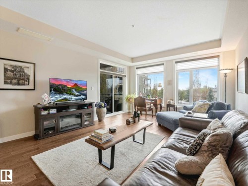 Living area featuring wood-finish flooring, light-toned walls, and a sliding glass door providing access to an outdoor space - 213 625 Leger Way, Edmonton, AB - Indoor Photo Showing Living Room