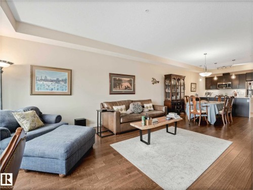 Open-concept living space featuring wood-finish flooring, recessed lighting, and tray ceiling details - 213 625 Leger Way, Edmonton, AB - Indoor Photo Showing Living Room