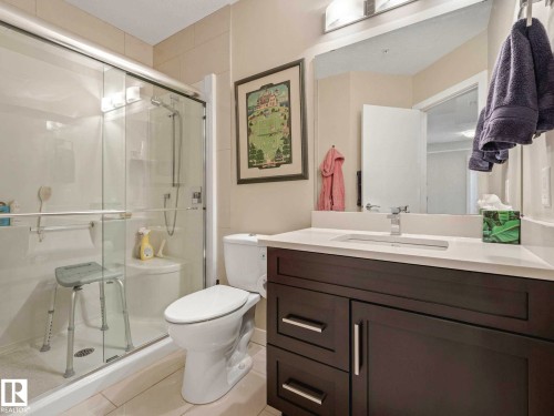 Contemporary bathroom featuring a dark wood-finish vanity with a white countertop and undermount sink - 213 625 Leger Way, Edmonton, AB - Indoor Photo Showing Bathroom