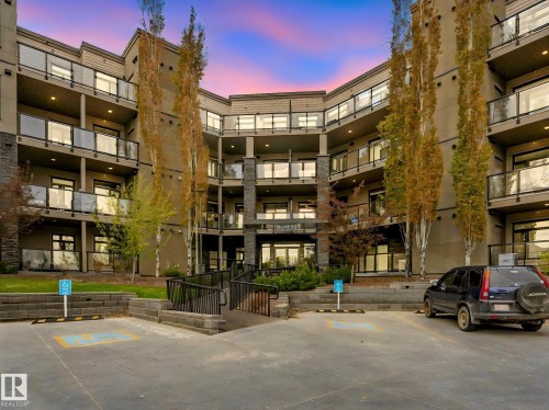 Contemporary multi-story building featuring a stucco and stone facade, private balconies with glass railings, and a main entrance with an accessible ramp - 213 625 Leger Way, Edmonton, AB - Outdoor With Balcony
