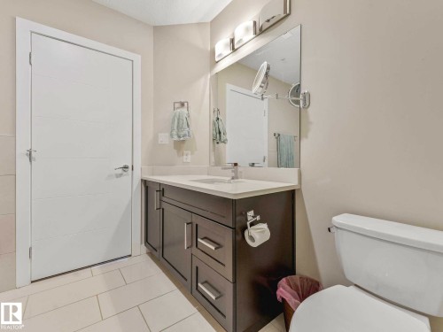 Bathroom featuring a dark wood-finish vanity with a light countertop, integrated sink, and an expansive mirror - 213 625 Leger Way, Edmonton, AB - Indoor Photo Showing Bathroom