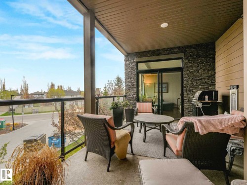 Expansive outdoor patio featuring a concrete surface, glass railing, stone accent wall, and sliding glass doors - 213 625 Leger Way, Edmonton, AB - Outdoor With Balcony With Exterior