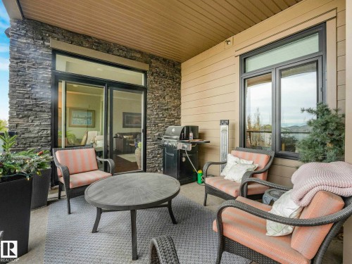 Covered patio featuring stacked stone accents and neutral siding - 213 625 Leger Way, Edmonton, AB - Outdoor With Deck Patio Veranda With Exterior