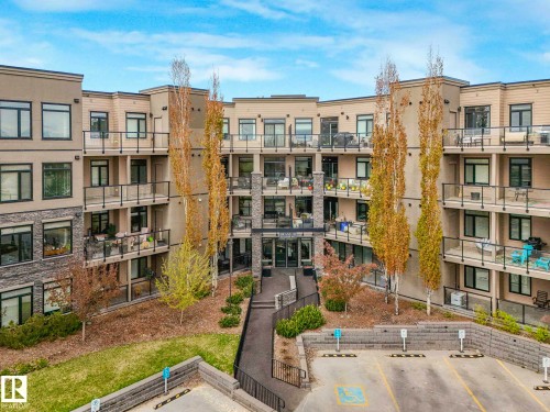 Multi-story building featuring a stone and siding exterior, private balconies with glass railings, and expansive windows - 213 625 Leger Way, Edmonton, AB - Outdoor With Balcony
