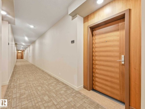Entry door featuring a natural wood finish with horizontal detailing, framed by a light wood trim - 213 625 Leger Way, Edmonton, AB - Indoor Photo Showing Other Room