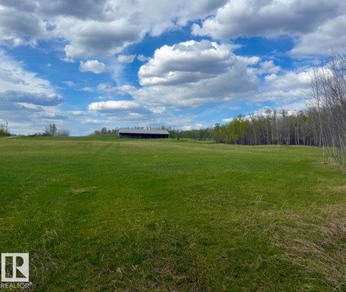 Expansive green field featuring a large agricultural building with a metal roof, surrounded by mature trees - 50206 Range Road 215, Rural Leduc County, AB 