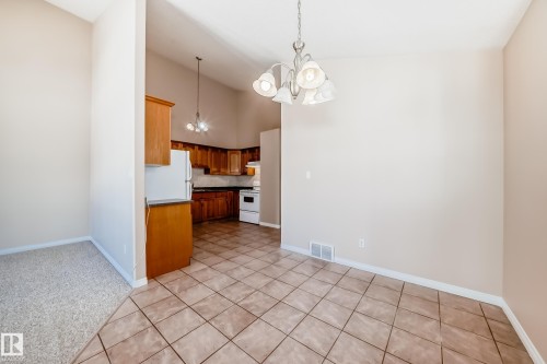 Open-concept dining area with tile flooring and a multi-arm chandelier, extending into a kitchen featuring wooden cabinetry, dark countertops, and white appliances - 9825 156 Street, Edmonton, AB - Indoor Photo Showing Kitchen