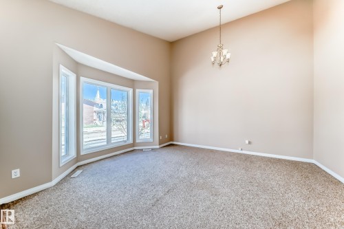 Spacious room featuring a prominent bay window with white trim, neutral wall paint, and a textured carpeted floor - 9825 156 Street, Edmonton, AB - Indoor Photo Showing Other Room