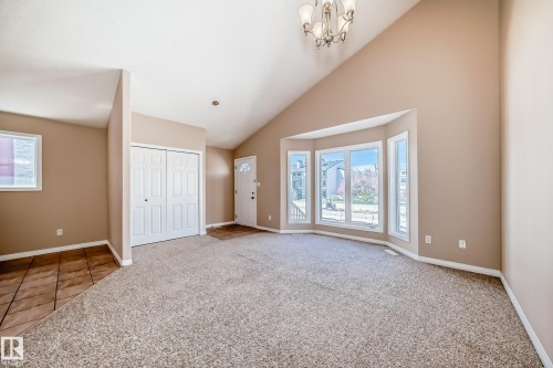 Vaulted ceiling living area featuring a bay window, carpeted flooring, a chandelier fixture, and a front entry door with glass insert - 9825 156 Street, Edmonton, AB - Indoor Photo Showing Other Room