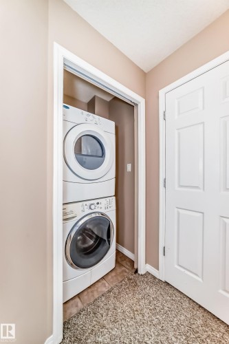 Dedicated laundry closet with stacked washer and dryer, finished with neutral wall paint and a tile floor base - 9825 156 Street, Edmonton, AB - Indoor Photo Showing Laundry Room
