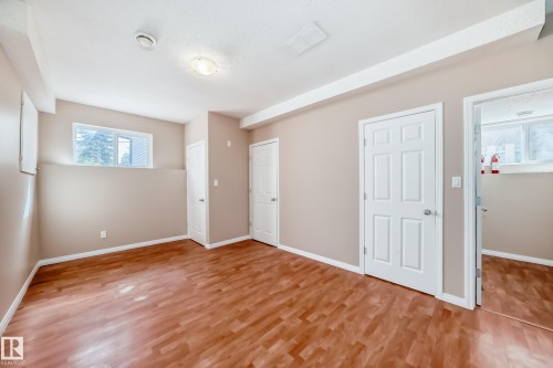 Spacious room featuring wood-finish flooring, light tan walls, multiple white panel doors, and two windows providing natural light - 9825 156 Street, Edmonton, AB - Indoor Photo Showing Other Room