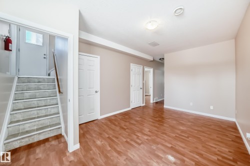 Spacious interior featuring wood-finish flooring, neutral-toned walls, white trim, and a tile staircase - 9825 156 Street, Edmonton, AB - Indoor Photo Showing Other Room