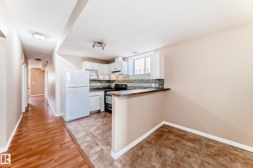 Kitchen area featuring white cabinetry, a mosaic tile backsplash, and a breakfast bar with a stone-finish countertop - 9825 156 Street, Edmonton, AB - Indoor Photo Showing Kitchen