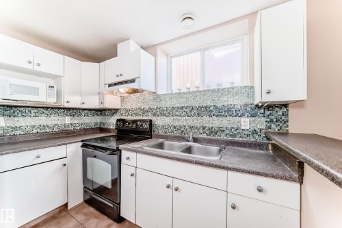 Kitchen featuring white cabinetry, black appliances, a mosaic tile backsplash, a double basin stainless steel sink, and a built-in microwave - 9825 156 Street, Edmonton, AB - Indoor Photo Showing Kitchen With Double Sink