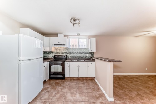 Kitchen featuring white cabinetry, dark countertops, tile flooring, and a mosaic tile backsplash - 9825 156 Street, Edmonton, AB - Indoor Photo Showing Kitchen With Double Sink