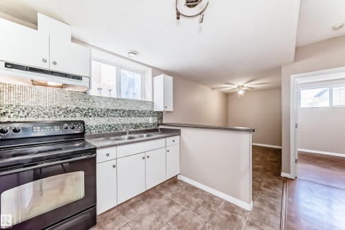 Kitchen featuring white cabinetry, a black electric range, a mosaic tile backsplash, a double basin sink, and tile flooring - 9825 156 Street, Edmonton, AB - Indoor Photo Showing Kitchen With Double Sink