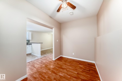 Interior space featuring wood-finish flooring, a ceiling fan with integrated lighting, and an open doorway providing access to a kitchen area with white cabinetry and a breakfast bar - 9825 156 Street, Edmonton, AB - Indoor Photo Showing Other Room