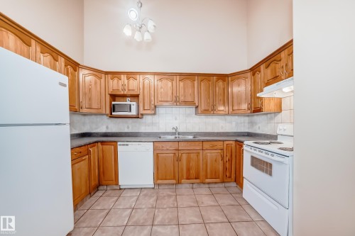 Kitchen featuring extensive wood cabinetry, tile flooring, and white appliances - 9825 156 Street, Edmonton, AB - Indoor Photo Showing Kitchen With Double Sink