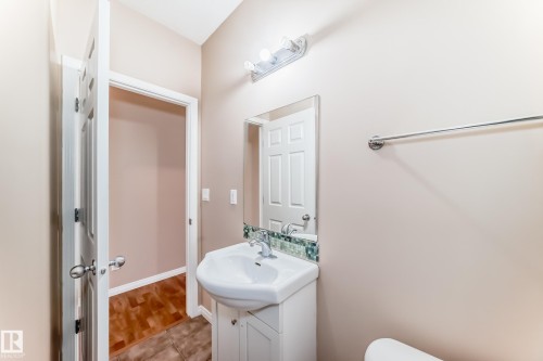 Bathroom featuring a white pedestal sink with chrome faucet, mirror with decorative tile backsplash, and overhead vanity lighting - 9825 156 Street, Edmonton, AB - Indoor Photo Showing Bathroom