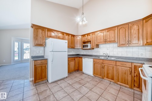 Kitchen featuring wood cabinetry, laminate countertops, tile flooring, and a vaulted ceiling with a chandelier - 9825 156 Street, Edmonton, AB - Indoor Photo Showing Kitchen