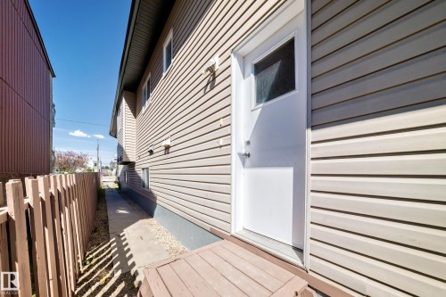Side exterior entry featuring a solid white door with an upper window insert, wood-finish steps, and light-colored horizontal siding - 9825 156 Street, Edmonton, AB - Outdoor With Exterior