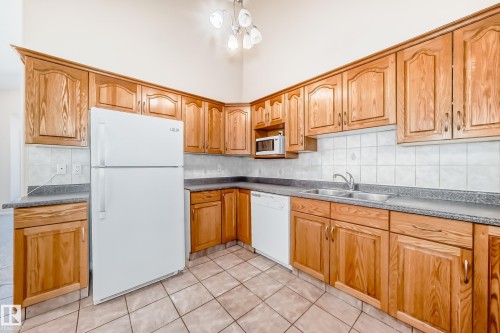 Kitchen featuring extensive wood cabinetry, tile flooring, white appliances, and a dual-basin sink - 9825 156 Street, Edmonton, AB - Indoor Photo Showing Kitchen With Double Sink