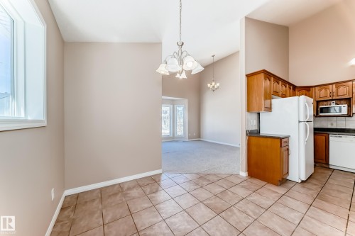 Kitchen and dining area featuring wood cabinetry, white appliances, dark countertops, and ceramic tile flooring - 9825 156 Street, Edmonton, AB - Indoor Photo Showing Kitchen