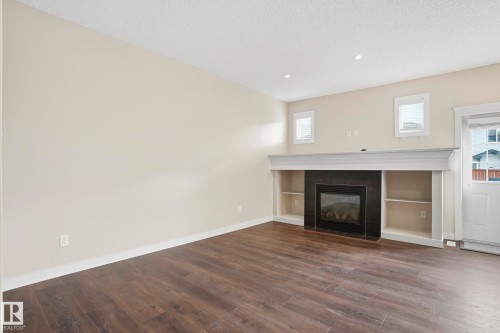 Living area featuring a dark wood-finish floor, a fireplace with a black surround, built-in shelving, white trim, and recessed lighting - 2917 16A Avenue, Edmonton, AB - Indoor Photo Showing Living Room With Fireplace