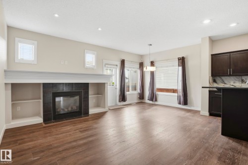 Living area featuring a central fireplace with black tile surround and integrated shelving, wood-finish flooring, recessed lighting, and a modern pendant light fixture - 2917 16A Avenue, Edmonton, AB - Indoor Photo Showing Living Room With Fireplace