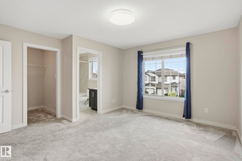 Carpeted room featuring a large window, a built-in closet with shelving, and an en-suite bathroom with a dark wood-finish vanity - 2917 16A Avenue, Edmonton, AB - Indoor