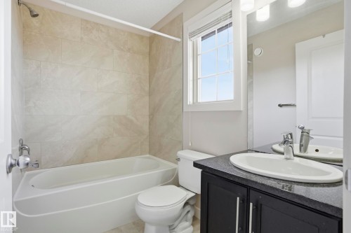 Bathroom featuring a white tub with ceramic tile surround, black vanity with a dark countertop, an oval undermount sink, and a window with white trim - 2917 16A Avenue, Edmonton, AB - Indoor Photo Showing Bathroom