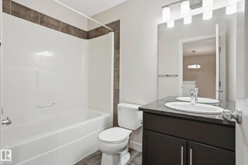Contemporary bathroom featuring a white tub/shower combination with dark accent tiling, a dark wood-finish vanity with a light speckled countertop, an undermount sink, and a large wall-mounted mirror - 2917 16A Avenue, Edmonton, AB - Indoor Photo Showing Bathroom