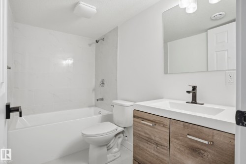 Modern bathroom featuring a wood-finish vanity with a white countertop and integrated sink, matte black faucet, and a tub/shower combination with white tile surround - 2917 16A Avenue, Edmonton, AB - Indoor Photo Showing Bathroom