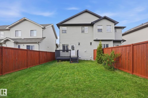 Expansive rear lawn featuring a dark wood deck, white egress door, and full perimeter wood fencing - 2917 16A Avenue, Edmonton, AB - Outdoor