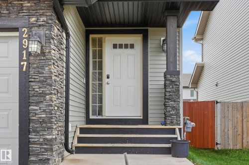 Entryway featuring stacked stone accents, light-colored siding, a white front door with upper lites, and a dark-stained wood porch column - 2917 16A Avenue, Edmonton, AB - Outdoor