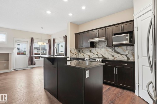 Kitchen featuring dark wood cabinetry, a granite island with an undermount sink, a stainless steel range hood, and a striking marble-look backsplash - 2917 16A Avenue, Edmonton, AB - Indoor Photo Showing Kitchen With Upgraded Kitchen