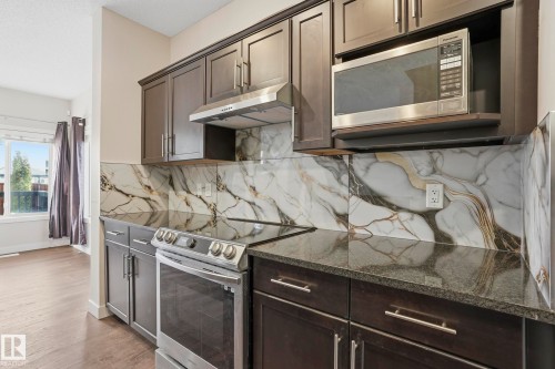 Kitchen featuring dark wood cabinetry, stainless steel appliances, dark stone countertops, and a striking marble-patterned backsplash - 2917 16A Avenue, Edmonton, AB - Indoor Photo Showing Kitchen