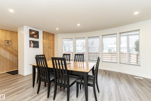 Spacious dining area featuring wood-finish flooring, a curved wall with multiple windows, recessed lighting, and a decorative slatted wood accent wall - 17716 84 Ave, Edmonton, AB - Indoor Photo Showing Dining Room