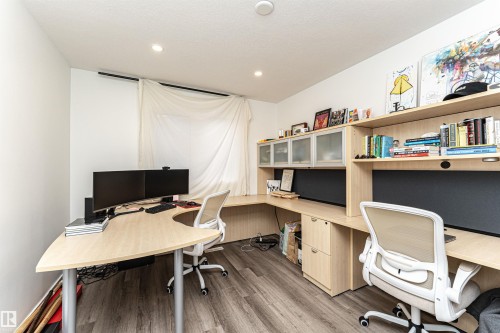 Office space featuring light wood-finish built-in desks, overhead shelving, and integrated cabinetry with frosted glass doors - 17716 84 Ave, Edmonton, AB - Indoor Photo Showing Office