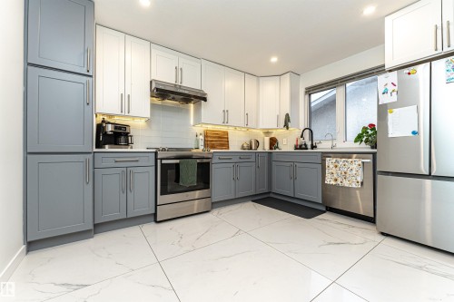 Contemporary kitchen featuring two-tone cabinetry, stainless steel appliances, a tile backsplash, and large format tile flooring - 17716 84 Ave, Edmonton, AB - Indoor Photo Showing Kitchen