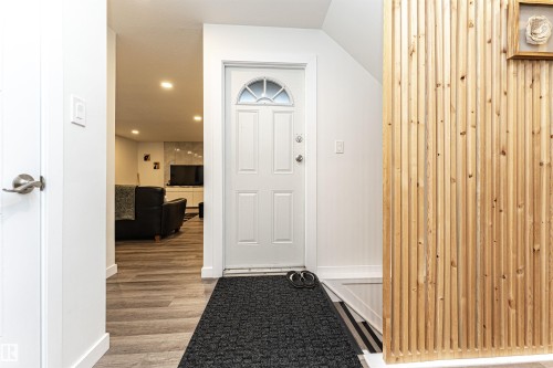 Entryway featuring a white paneled door with an arched glass insert, wood-finish flooring, recessed lighting, and a prominent vertical wood slat accent wall - 17716 84 Ave, Edmonton, AB - Indoor Photo Showing Other Room