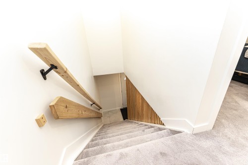 Carpeted staircase featuring natural wood handrails with matte black brackets, white baseboards, and a vertical wood slat accent wall - 17716 84 Ave, Edmonton, AB - Indoor Photo Showing Other Room
