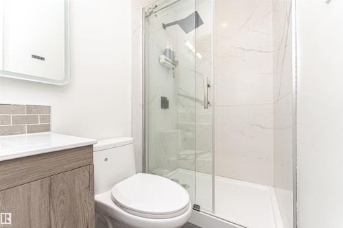 Modern bathroom featuring a glass-enclosed shower with white marble-look wall tiling, a wood-finish vanity with a white countertop, and a contemporary tile backsplash - 17716 84 Ave, Edmonton, AB - Indoor Photo Showing Bathroom
