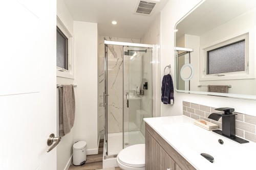 Contemporary bathroom featuring a walk-in shower with marble-look tile, a modern vanity with integrated sink, a rectangular framed mirror, and wood-finish flooring - 17716 84 Ave, Edmonton, AB - Indoor Photo Showing Bathroom
