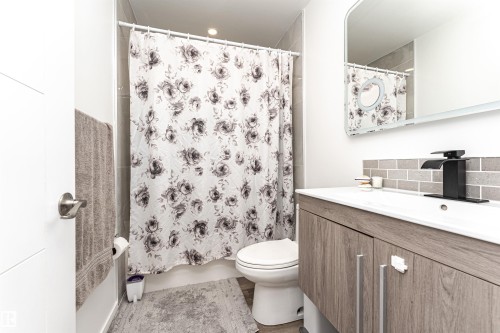 Bathroom featuring a wood-finish vanity with an integrated sink, a black waterfall-style faucet, and subway tile backsplash - 17716 84 Ave, Edmonton, AB - Indoor Photo Showing Bathroom