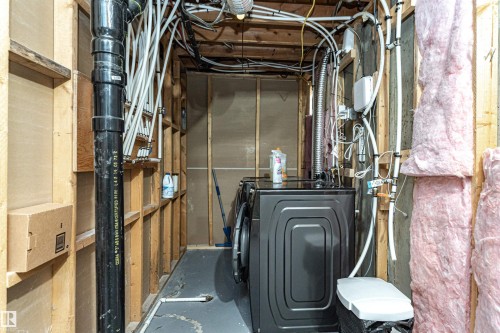 Utility area featuring visible structural framing, exposed plumbing, and a dark-finish washer and dryer unit - 17716 84 Ave, Edmonton, AB - Indoor
